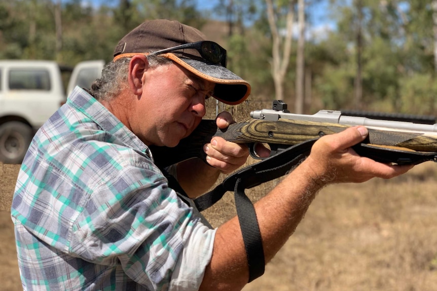 A middle-aged man, seen in profile, aims a rifle.