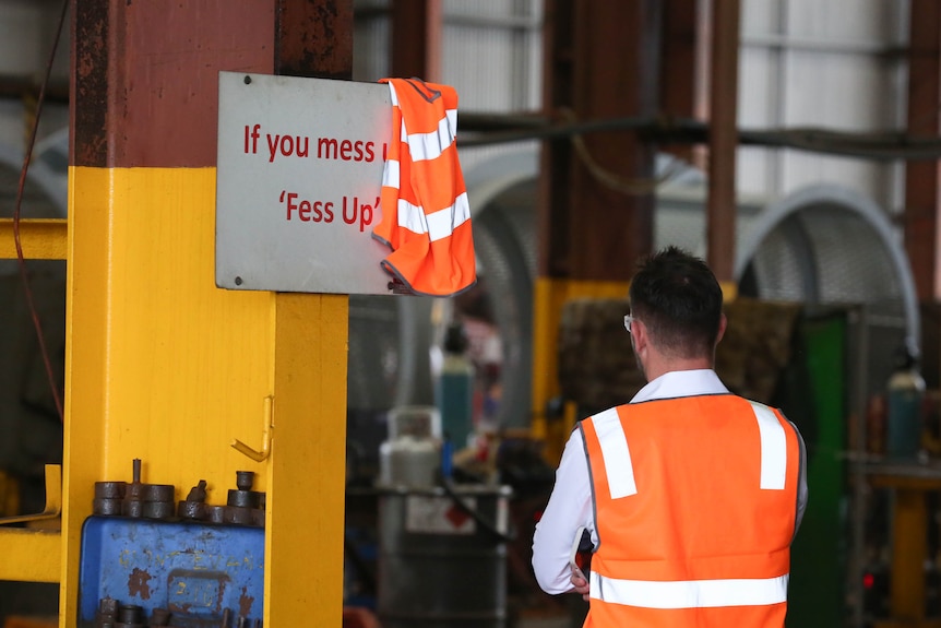 a hi vis vest half draped over a sign that reads 'if you mess up 'fess up'