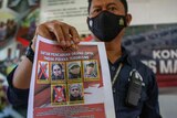 A police officer shows a wanted poster displaying the photos of two militants who were killed