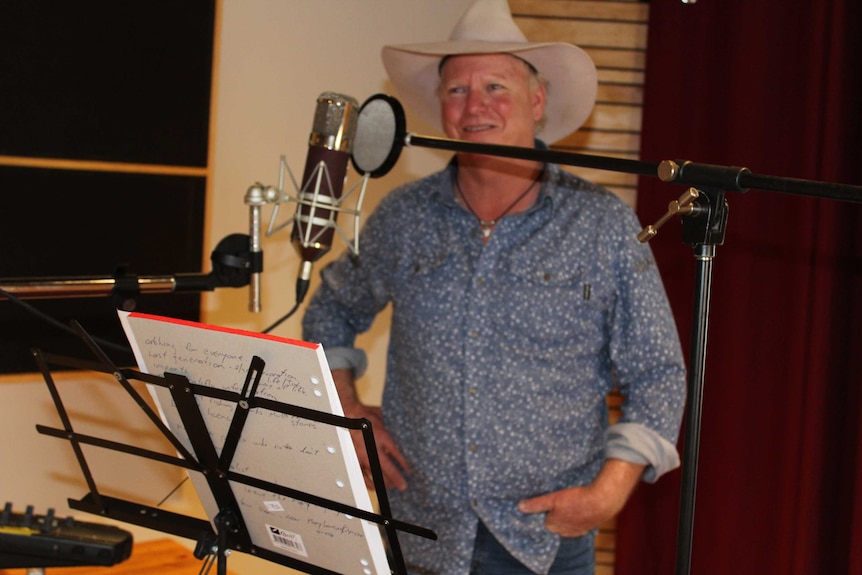 Fisherman and country music artist Ian Quinn stands in front of a microphone in a recording studio.