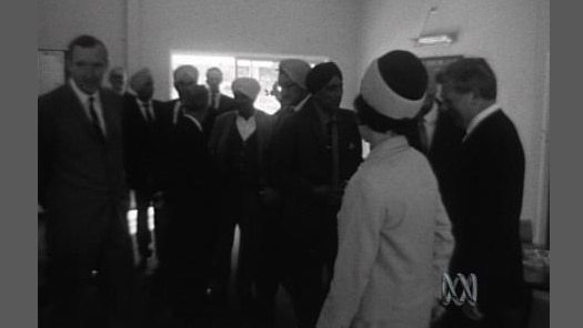 A group Sikh people stand in a room with others