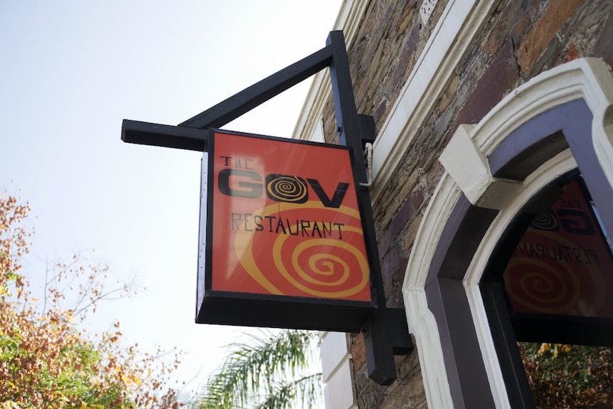 An orange sign attached to a building with the words "the gov restaurant"