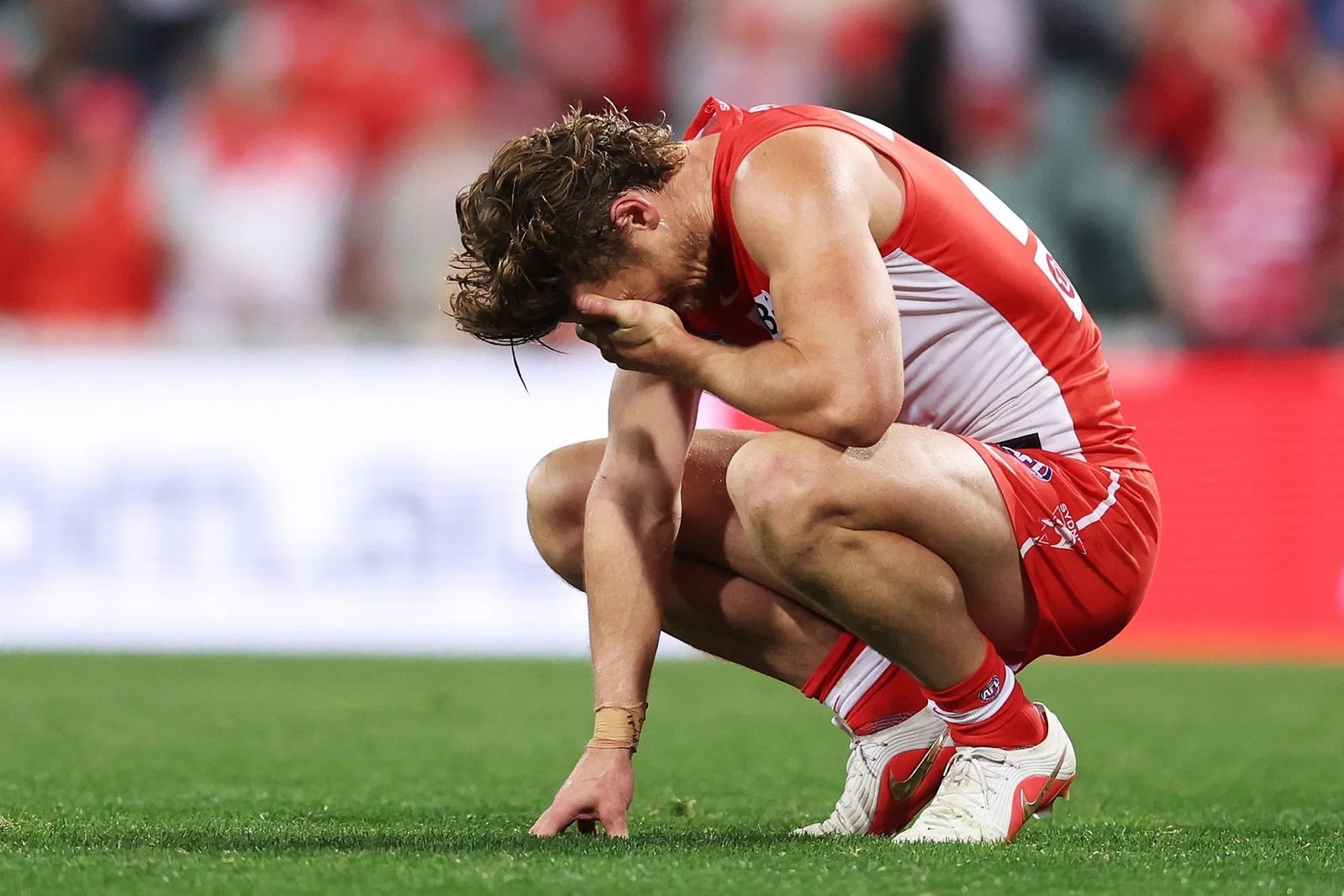 Dane Rampe of the Swans on his haunches, holding his head, crying on the field