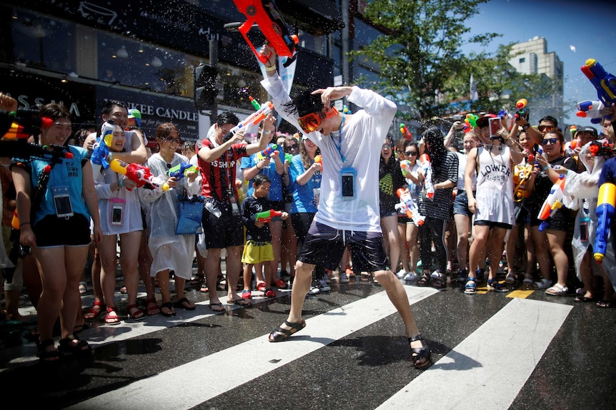Man dances while surrounded by people holding water guns on streets of Seoul