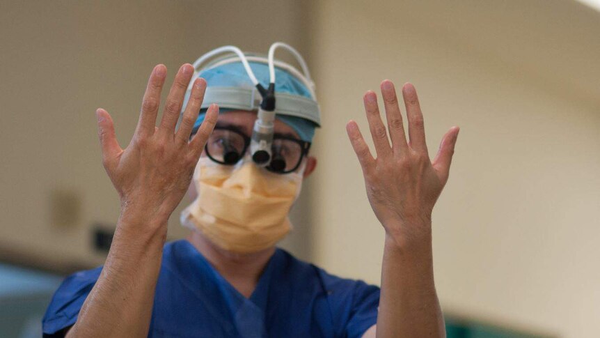 A surgeon with operating mask and gear on holds his hands up to the camera