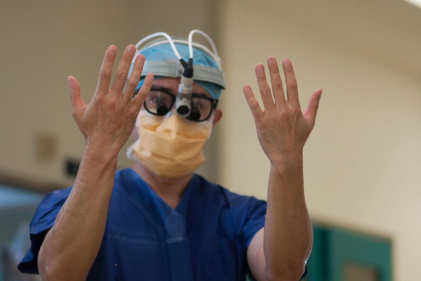 A surgeon with operating mask and gear on holds his hands up to the camera