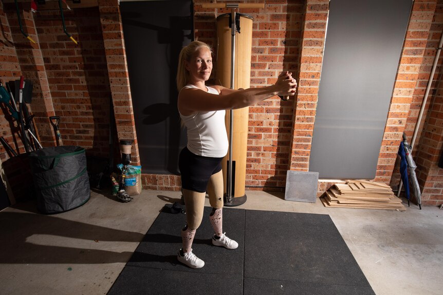 A blonde woman in workout clothing stands on a yoga mat.