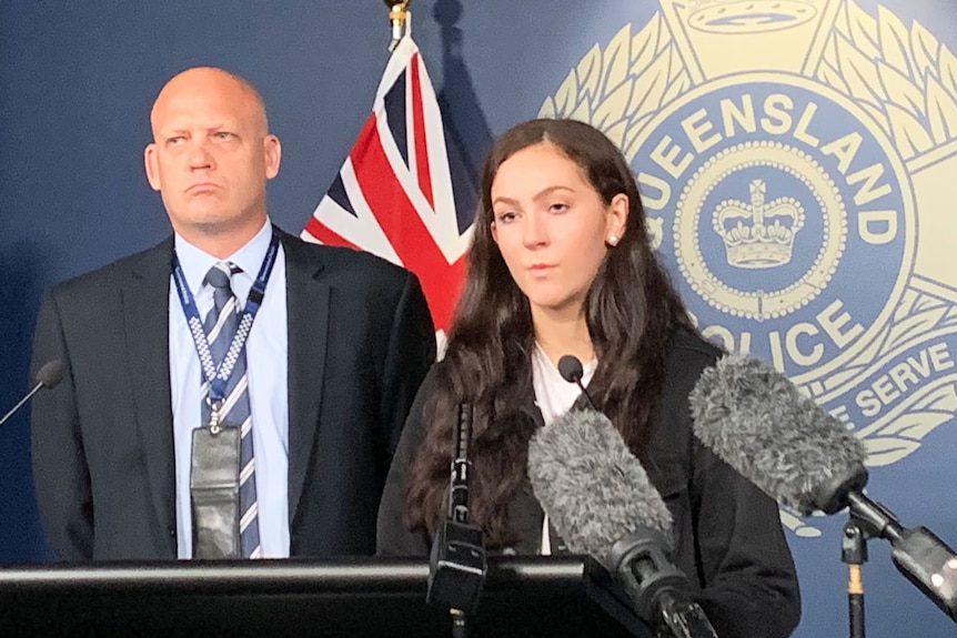 A young woman speaks at a police press conference flanked by an officer
