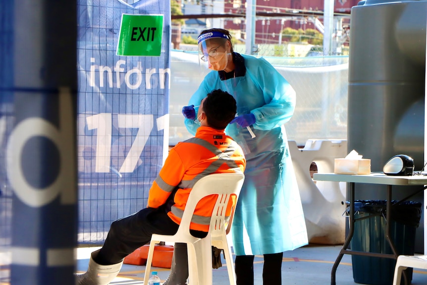 a tradesman at a building site having a swap put up their nose by a nurse