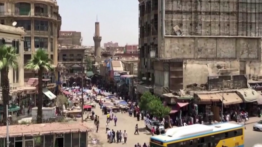 A busy Cairo street with buildings and palm trees surrounding people on a sunny day 