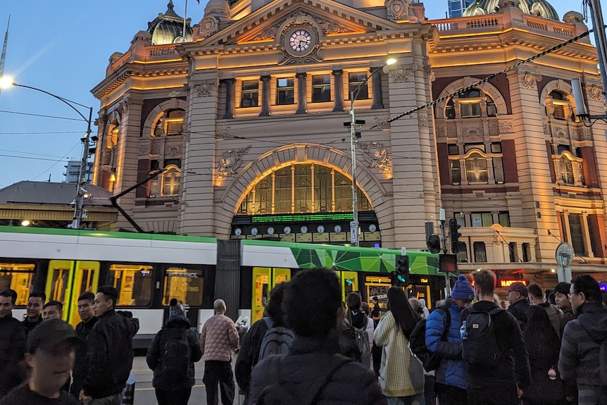 Pedestrians and a tram in front of a busy Flinders Street station in the early evening