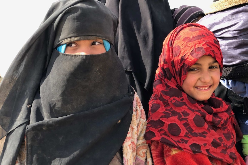 A woman and a girl wearing Islamic headdress  look away from the camera as they are photographed.