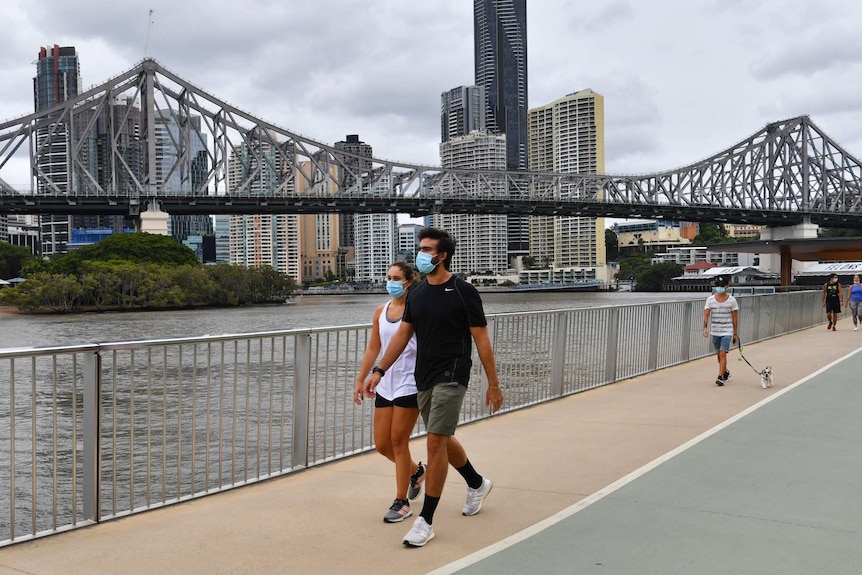 two people walk in face masks along a river.