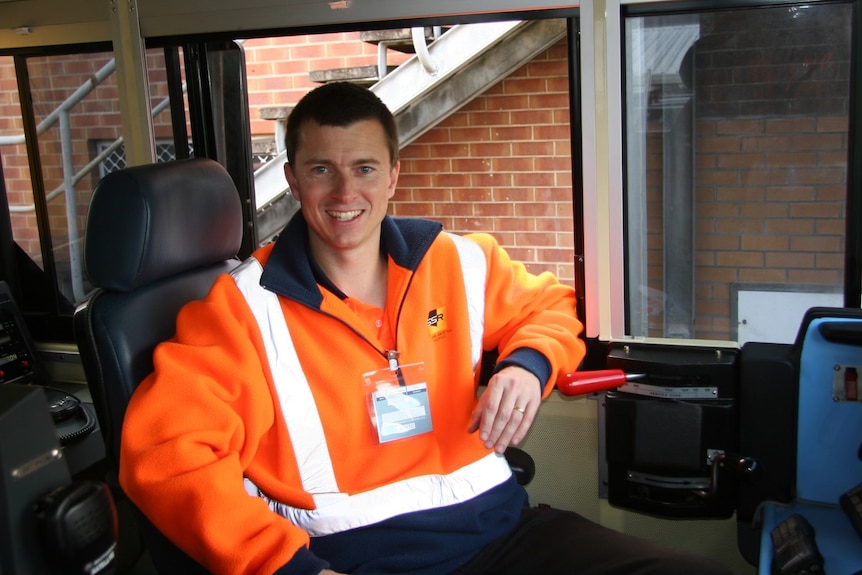 Man in Hi-Vis vest smiles at camera in cabin of train