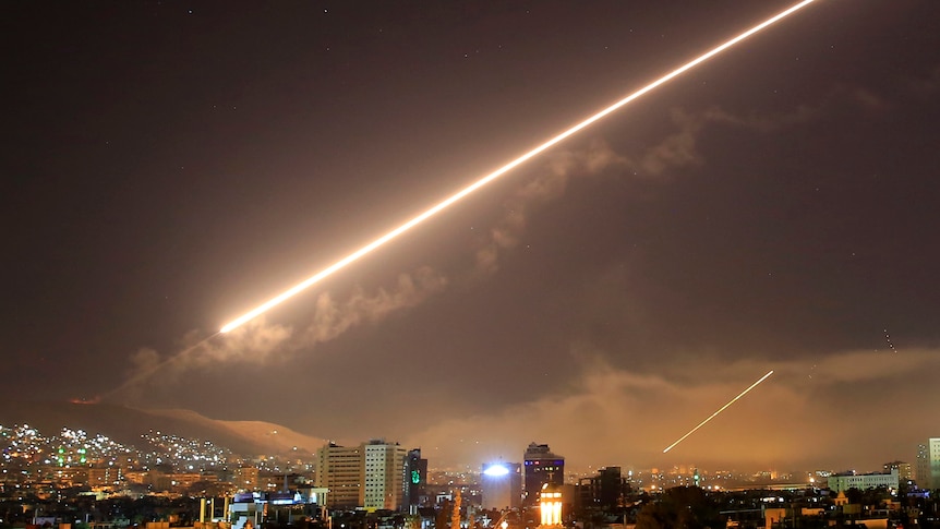 A streak of light arcs across the sky over a city.