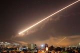 A streak of light arcs across the sky over a city.