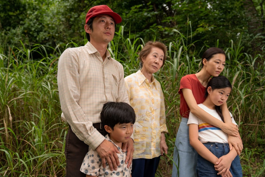 A still from the film Minari with a family: father, mother, grandmother and two young children, standing in a green field