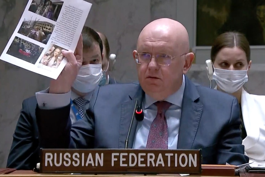 Russian Ambassador Vasily Nebenzya holds up copies of photos while speaking during a Security Council meeting.