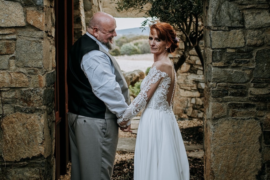 Couple smiles and holds hands on their wedding day, professional shot of woman with red hair up-do and wedding dress 