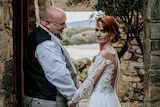 Couple smiles and holds hands on their wedding day, professional shot of woman with red hair up-do and wedding dress 