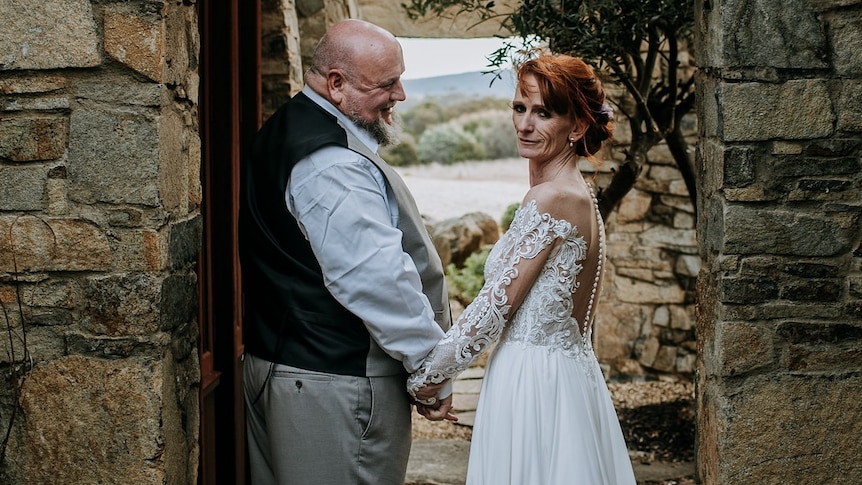 Couple smiles and holds hands on their wedding day, professional shot of woman with red hair up-do and wedding dress 
