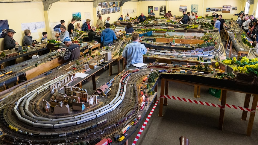 People looking at a large model railway set inside a large shed.