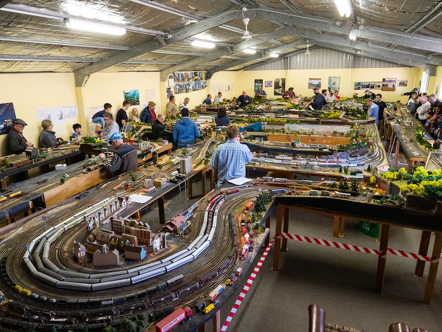 People looking at a large model railway set inside a large shed.