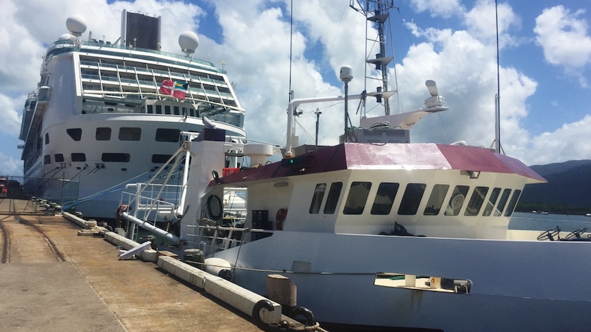 A prawn trawler is dwarfed when docked alongside an ocean cruise liner in the port of Cairn