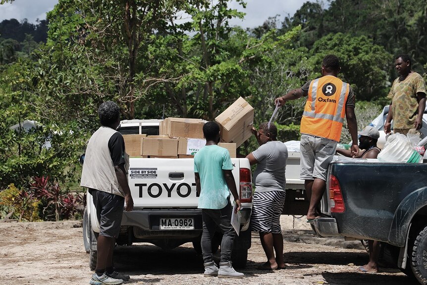 A group of people unload a ute with boxes.