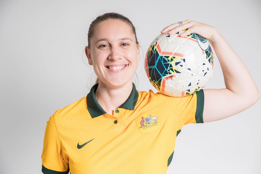 A female soccer player with disability holds a football and smiles at the camera