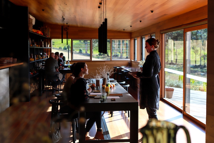 A light-filled dining room with two diners talking to a waitress in black clothing