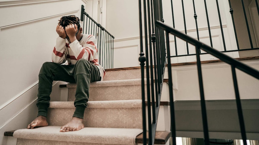 A young boy sits on stairs with his head in his hands