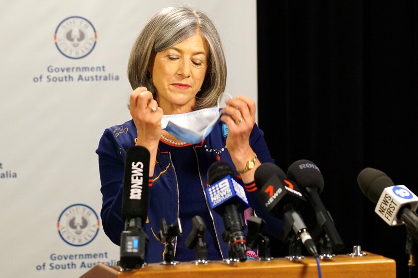 A woman standing in front of microphones removes a face mask