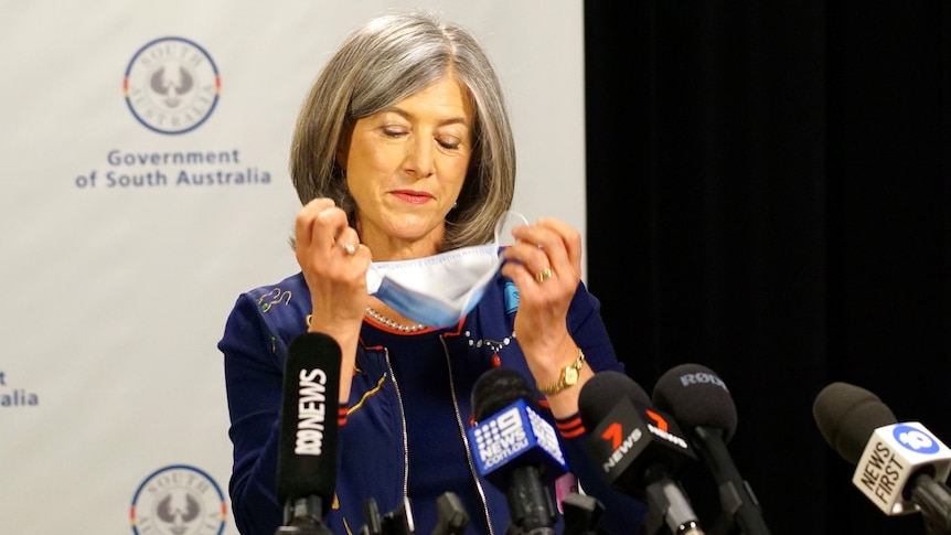 A woman standing in front of microphones removes a face mask