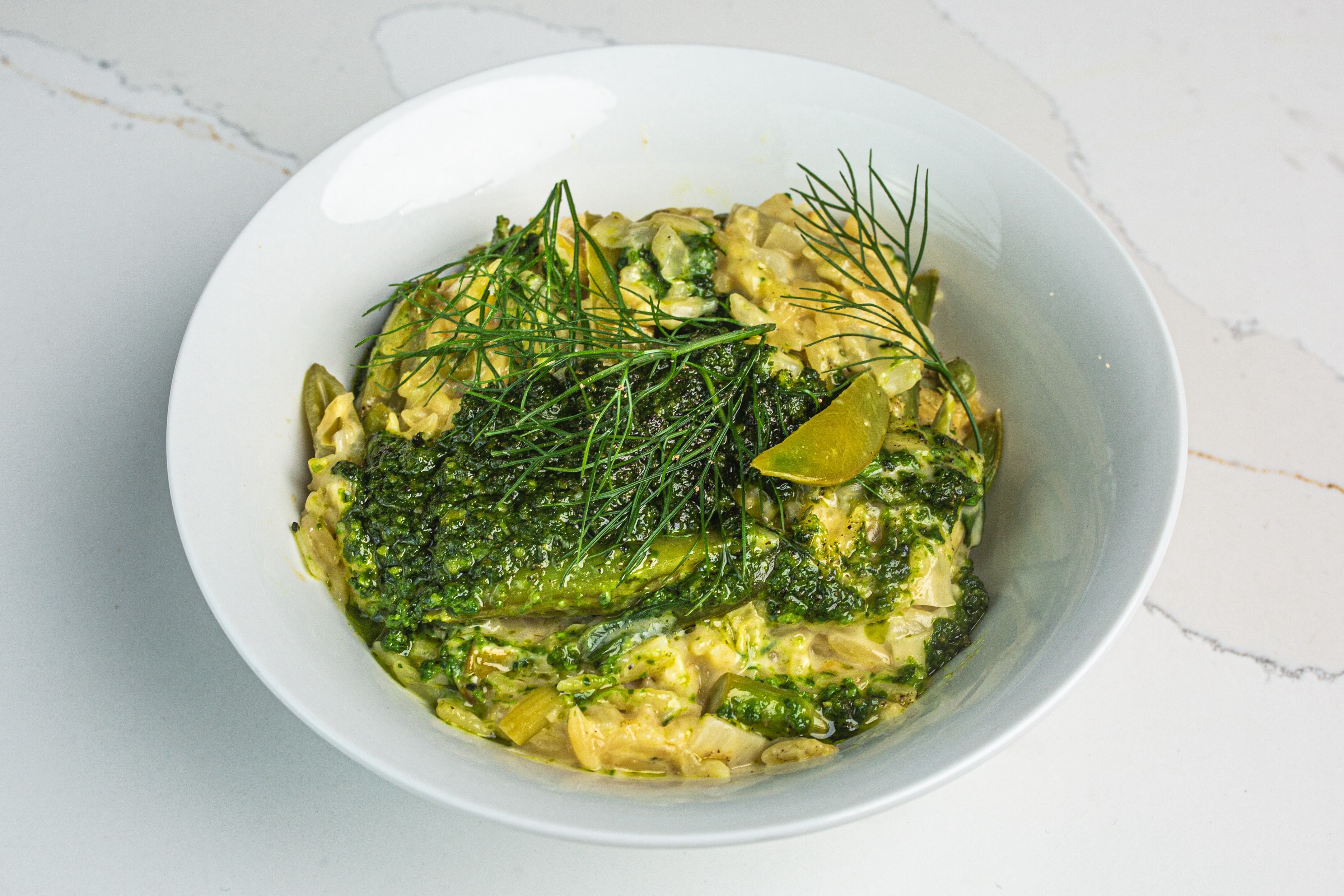 A bowl of creamy spring vegetable orzo with asparagus and sugar snap peas, topped with dill and pesto.