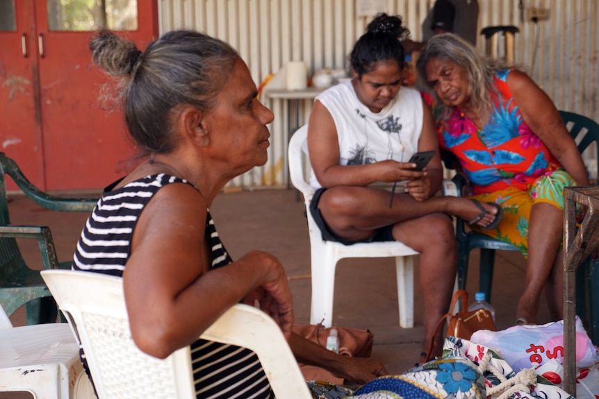 Three women are sitting on plastic chairs.