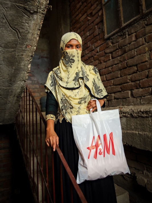 Fatima stands on stairs holding H&M shopping bag.