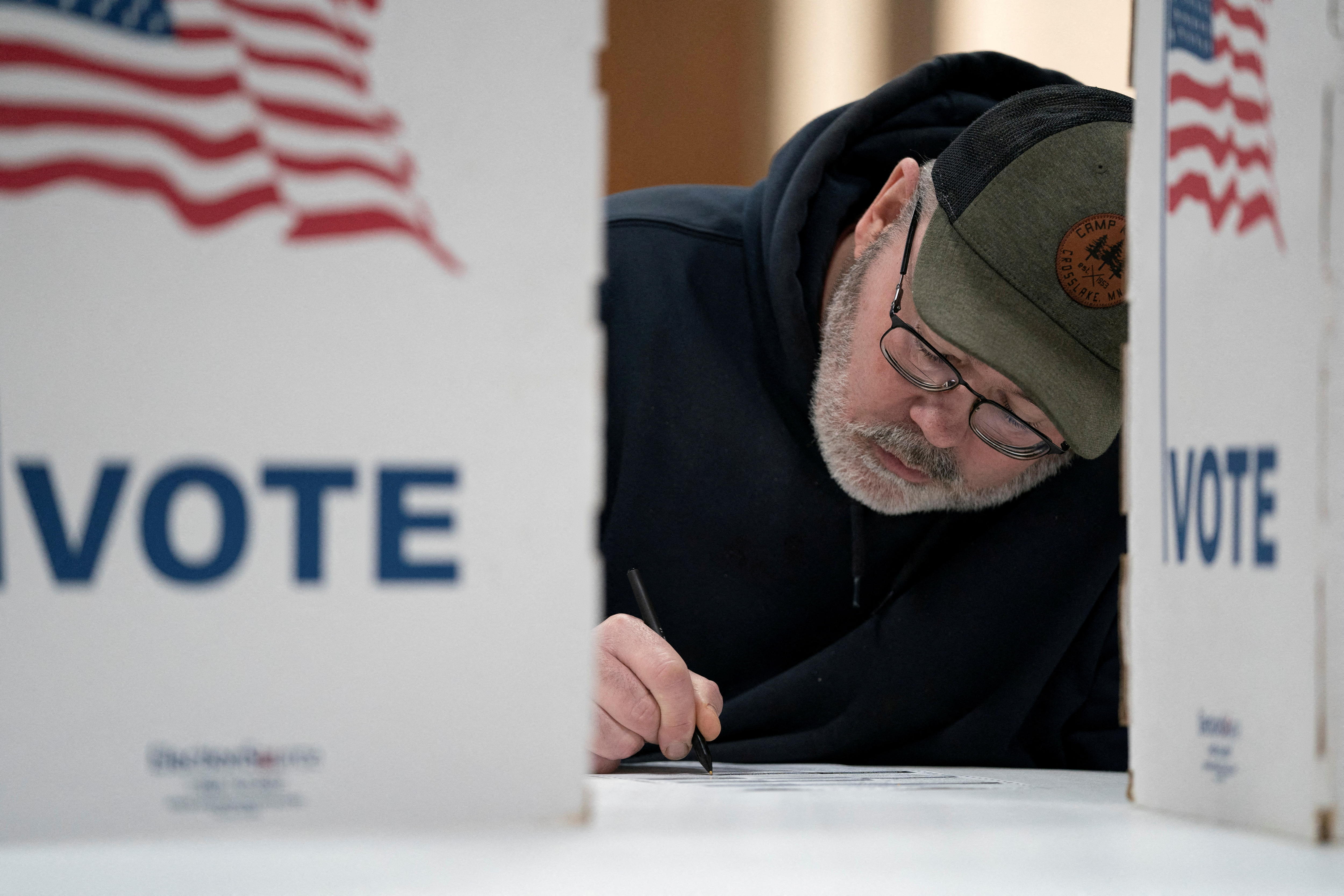 A man leans over a table where he is casting a vote.