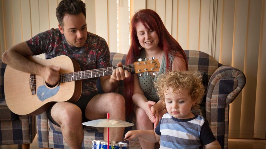 Chris Wright plays the guitar, alongside Jo Wright, as 2-year-old Philip Wright plays a kids' drum set in front of them.