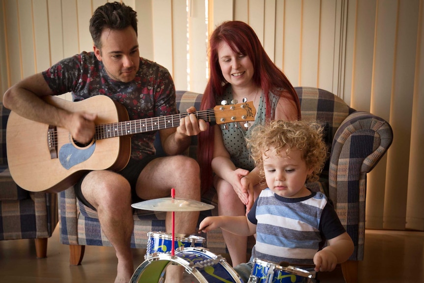 Chris Wright plays the guitar, alongside Jo Wright, as 2-year-old Philip Wright plays a kids' drum set in front of them.