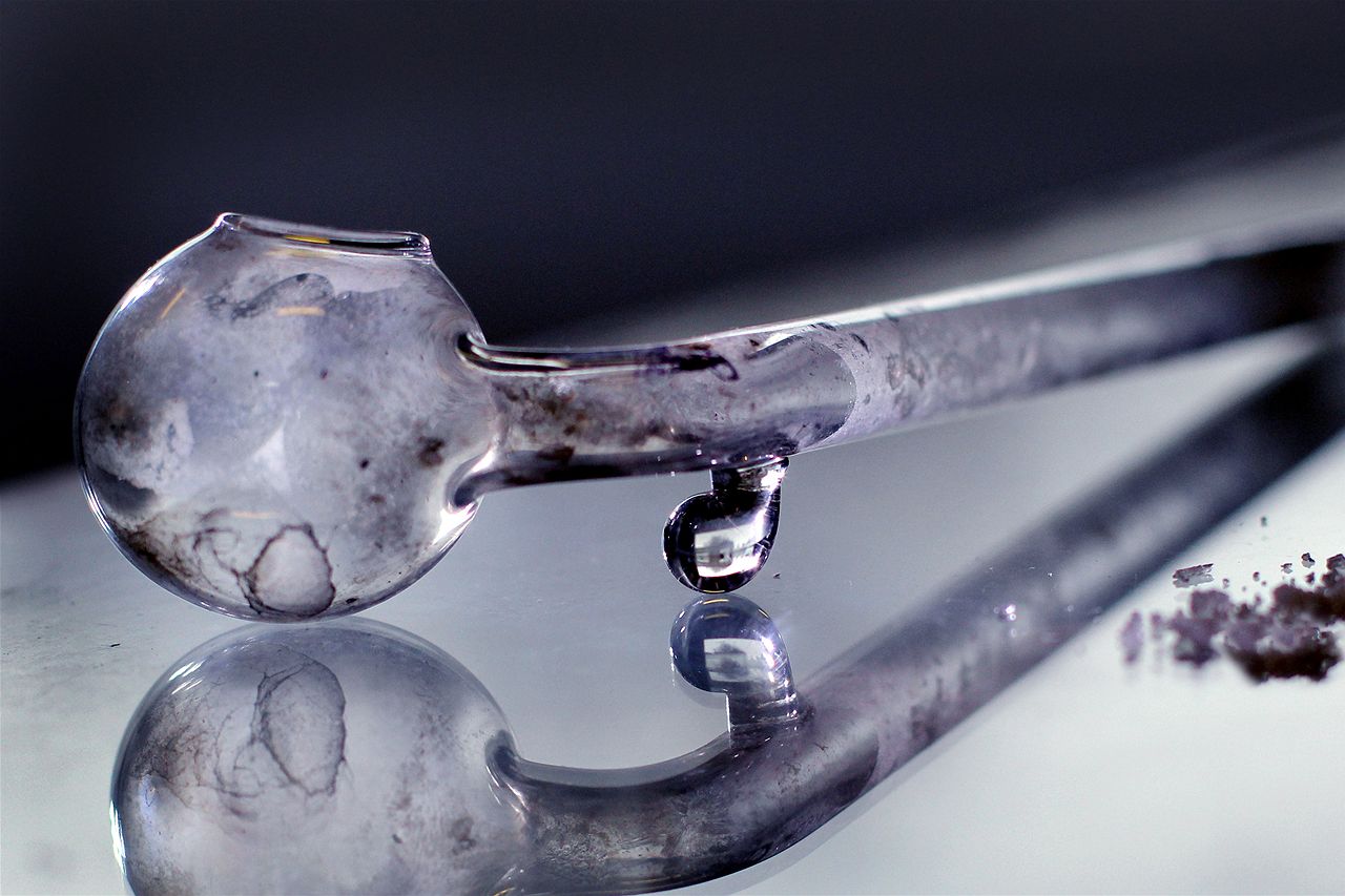 Um cachimbo de vidro sujo fica sobre uma superfície espelhada.