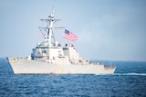 A US warship sails through the sea with an American flag raised.