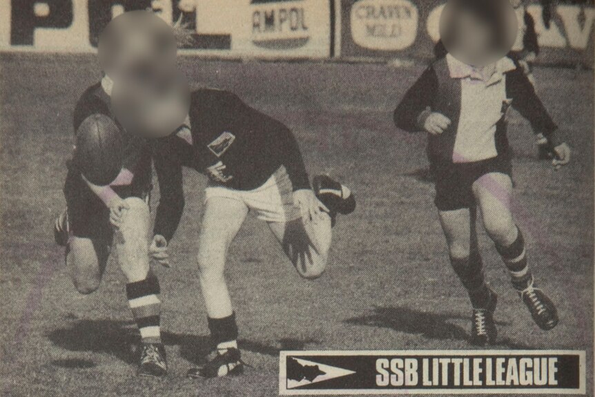 A black and white newspaper image of three boys in replica St Kilda uniforms playing Australian rules football.