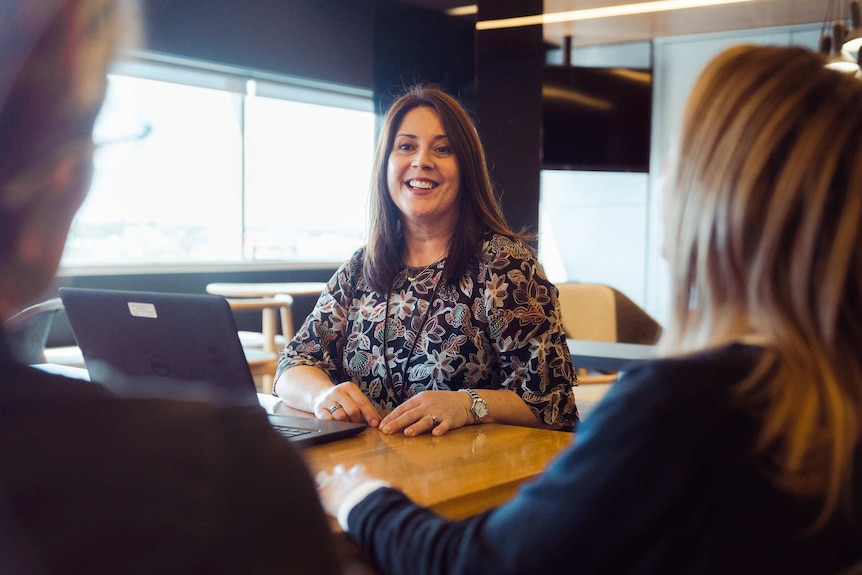 Sarah Rigby sits at a large office desk with two colleagues.