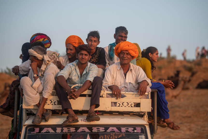 A group of about a dozen people sit on top of a truck.