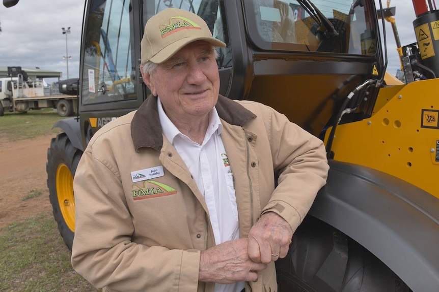 A man in a cream jacket leans on a tractor.