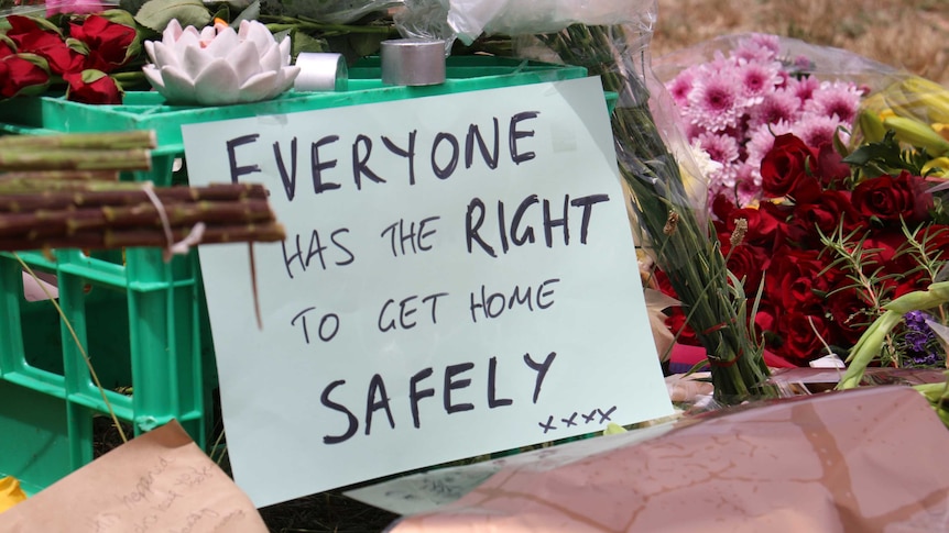Roses are laid over a milk crate with a sign reading 'everyone has the right to get home safely xxxx'