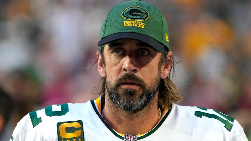 Bearded NFL quarterback Aaron Rodgers in gameday kit, wearing a Green Bay Packers cap.