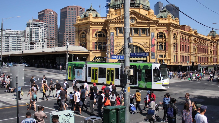 Pedestrians cross Flinders Street as a tram rumbles down Swanston Street outside Flinders Street Station.