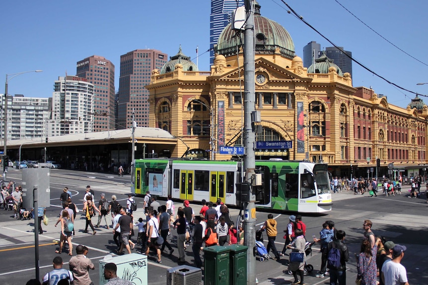 Pedestrians cross Flinders Street as a tram rumbles down Swanston Street outside Flinders Street Station.